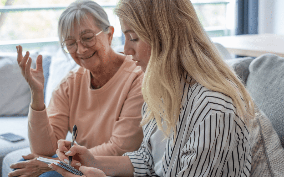 Grandmother and granddaughter sit on a sofa sharing a warm conversation while the younger woman takes notes in a notebook